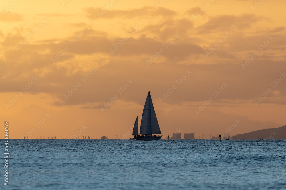 Incredible sunset on Waikiki Beach with sail boat silhouette. Sunset sailing in Hawaii.  