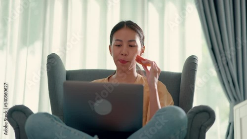 Young pretty woman sitting on sofa and eating apple while typing in laptop computer, new normal and working from home concept
