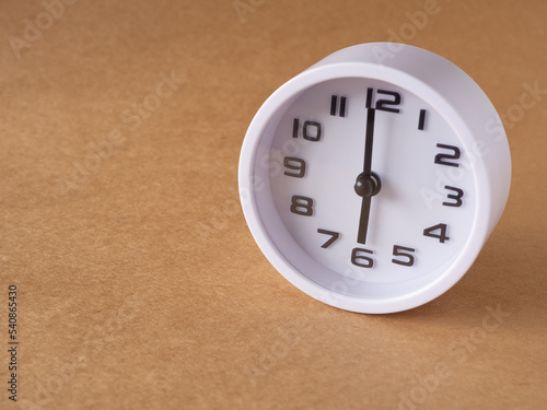 Close up, white clock shows time at 6 o'clock on the office brown workplace tabletop. Copy space for your text. Business and education concept..