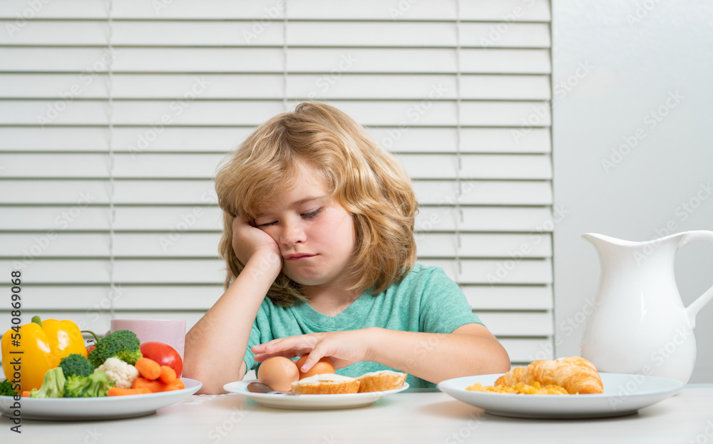 Portrait of kid with no appetite. Concept of loss of appetite. Funny blonde little boy having breakfast. Milk, vegetables and fruits healthy food nutrition for children. Portrait of kid with no appetite. Concept of loss of appetite. Funny blonde little boy having breakfast. Milk, vegetables and fruits healthy food nutrition for children.