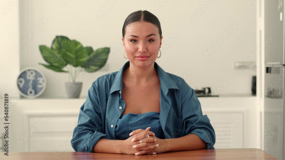Confident portrait of an attractive glamour young multi-ethnic woman in blue fashionable clothes, looking confidently at the camera, sitting at a table in a cozy white home interior. Front view Confident portrait of an attractive glamour young multi-ethnic woman in blue fashionable clothes, looking confidently at the camera, sitting at a table in a cozy white home interior. Front view
