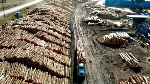 dolly forward wide drone shot over loaded logging semi truck driving forward between log piles at a sawmill in a desert environment photo