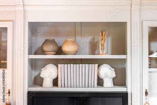 Schilderij op canvas Head shaped bookends with books and clay pot on a shelf indoors