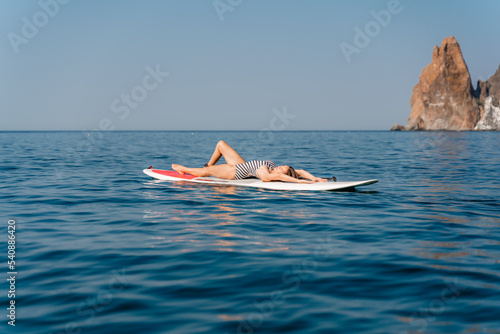 Sporty girl on a glanders surfboard in the sea on a sunny summer day. Summer activities by the sea