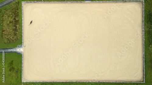 Flying above sport rider riding dark bay gelding showjumping over fence obstacles in big professional sandy parkour dressage arena. Horseman competing in equestrian jumping discipline