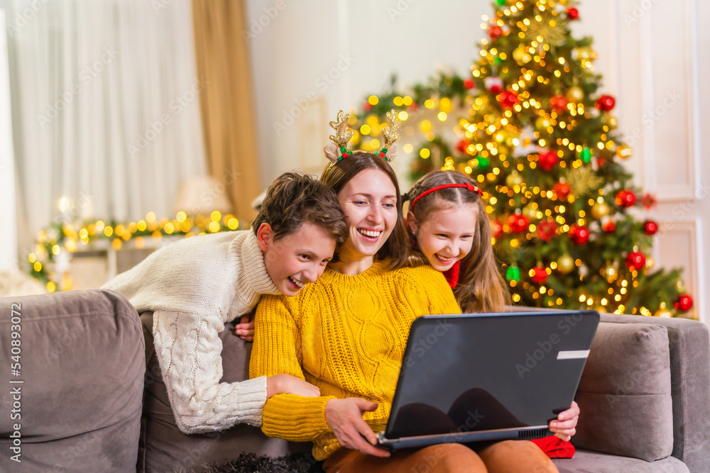 Portrait of a loving happy family sitting on the couch, using a laptop, calling video conferences with friends and family, watching funny videos of New Year's holidays. Shopping for Christmas sales Portrait of a loving happy family sitting on the couch, using a laptop, calling video conferences with friends and family, watching funny videos of New Year's holidays. Shopping for Christmas sales