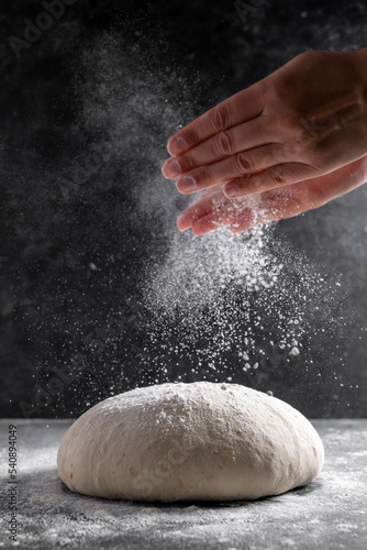 Raw dough and sprinklling flour over dark background. Cooking bread or pizza. Action, movement food photo