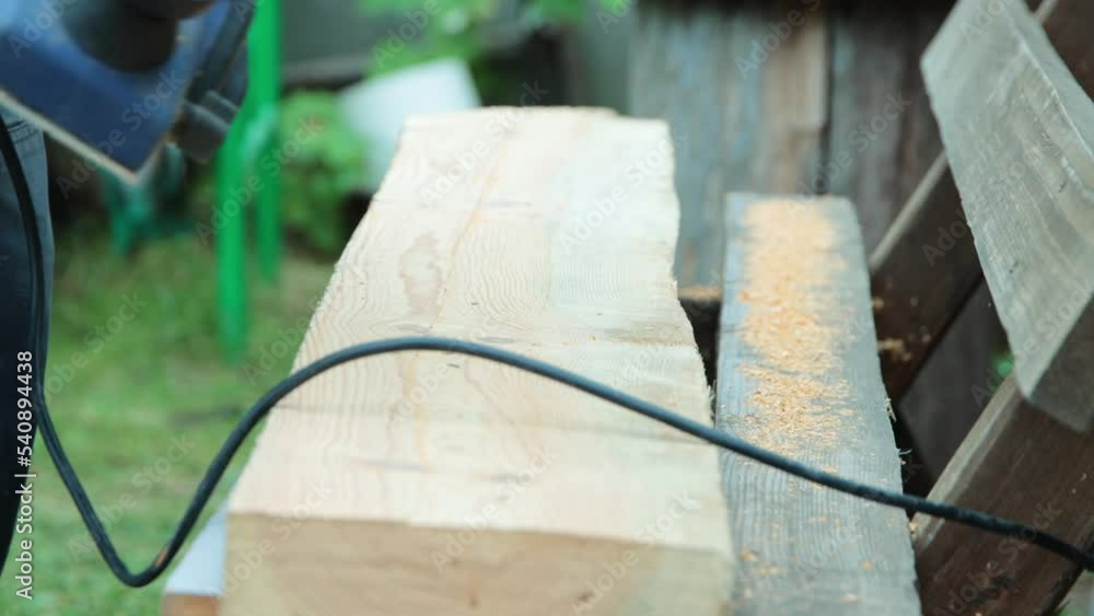 A male carpenter plans boards with an electric planer to make a bench. Carpentry, industry. Woodworker