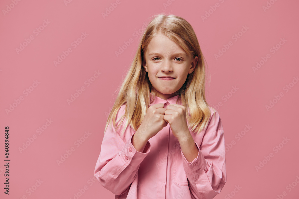 a serious, angry girl stands on a pink background in a pink shirt and holds her hands folded in fists a serious, angry girl stands on a pink background in a pink shirt and holds her hands folded in fists