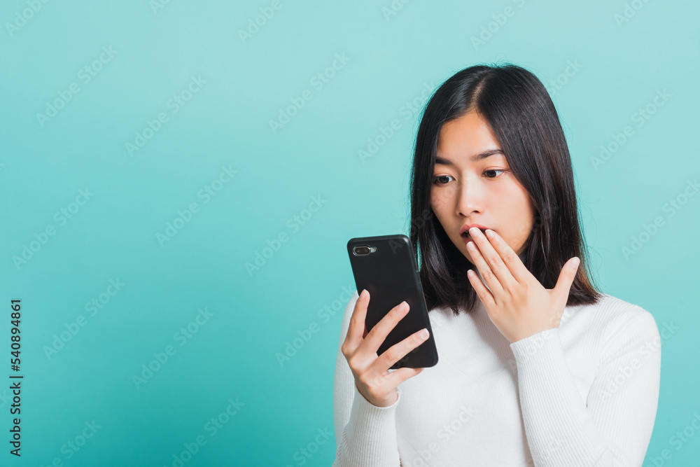 Portrait female anxious scared on the phone seeing bad news, Young beautiful Asian woman surprised shocked with mobile phone close mouth with palm, studio shot isolated on a blue background Portrait female anxious scared on the phone seeing bad news, Young beautiful Asian woman surprised shocked with mobile phone close mouth with palm, studio shot isolated on a blue background