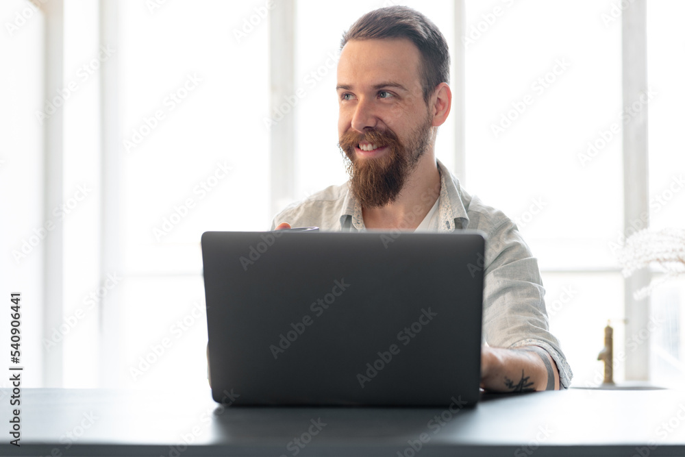 Stylish bearded man working on laptop from home sitting at the table Stylish bearded man working on laptop from home sitting at the table