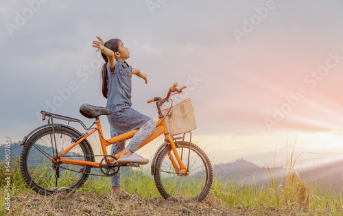 Happy little girl with bike at sunset on mountain
