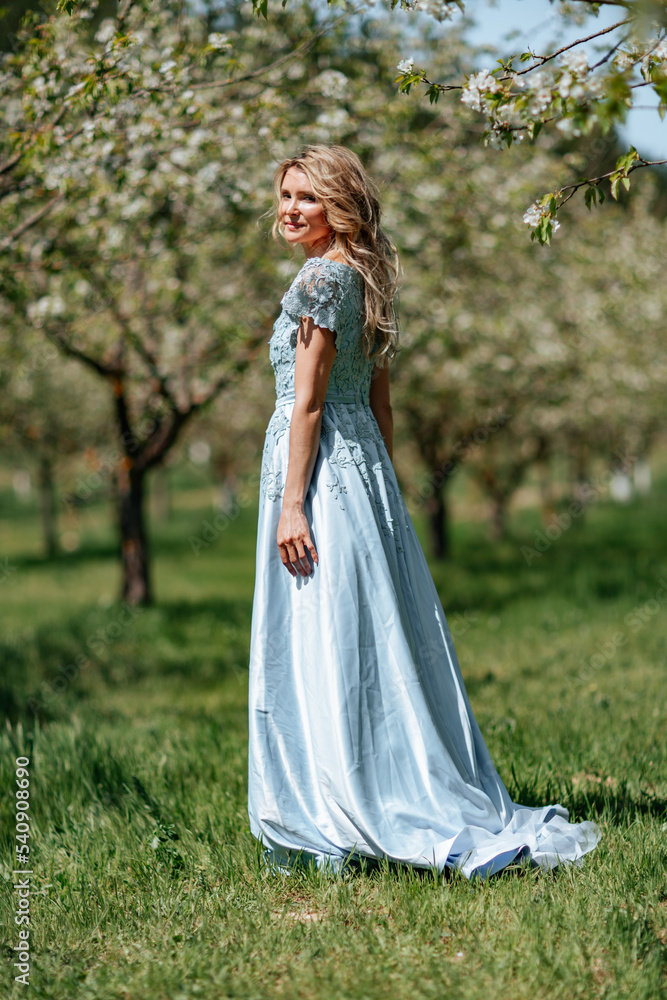 Portrait of a blonde in the park. Beautiful woman with long blond hair in a blue dress. Portrait of a blonde in the park. Beautiful woman with long blond hair in a blue dress.