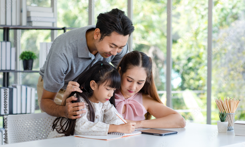 Millennial Asian happy family father and mother smiling helping supporting teaching little girl daughter studying learning writing doing school homework via tablet computer in living room at home Millennial Asian happy family father and mother smiling helping supporting teaching little girl daughter studying learning writing doing school homework via tablet computer in living room at home