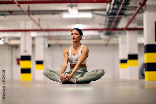 Flexible sporty girl stretching her legs in underground parking.