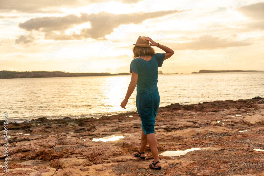 A young woman with a hat at sunset on the Paseo de Poniente in San Antonio Abad, Ibiza Island. Balearic
