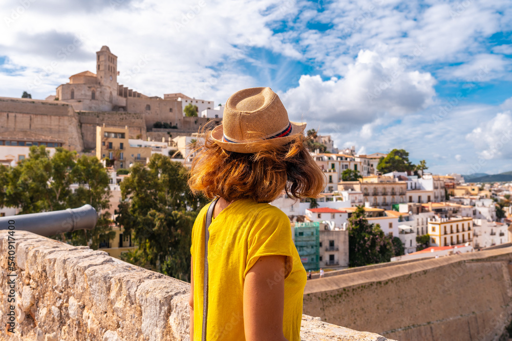 A young woman on vacation looking at the cathedral of Santa Maria de la Neu from the castle wall of Ibiza, Balearic Islands, Eivissa
