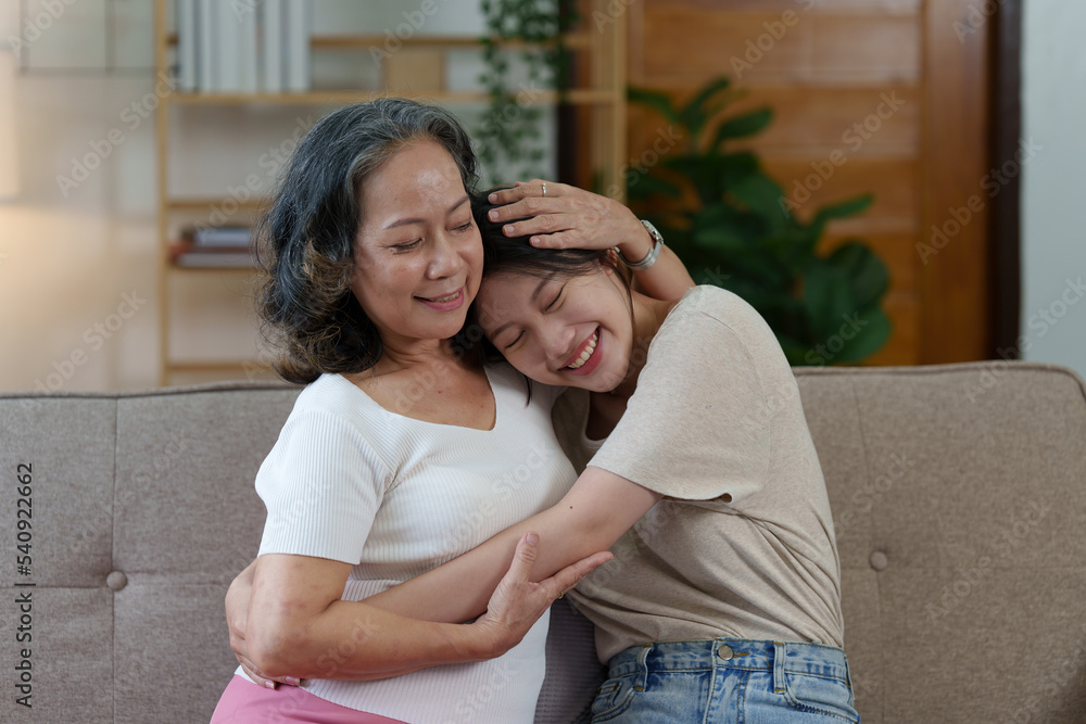 Happy senior Asian woman and her adult daughter are cuddling on the couch Happy senior Asian woman and her adult daughter are cuddling on the couch