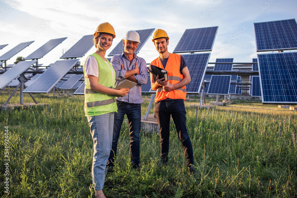 Charismatic group of investors and ecological engineer pretty woman all with safety helmets analysing the plan of work at photovoltaic solar panels farm Charismatic group of investors and ecological engineer pretty woman all with safety helmets analysing the plan of work at photovoltaic solar panels farm