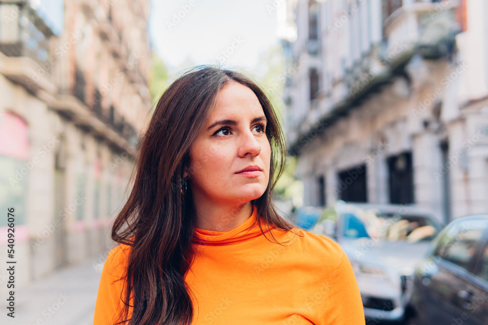 Woman in orange clothes walking through the streets of the city looking away.