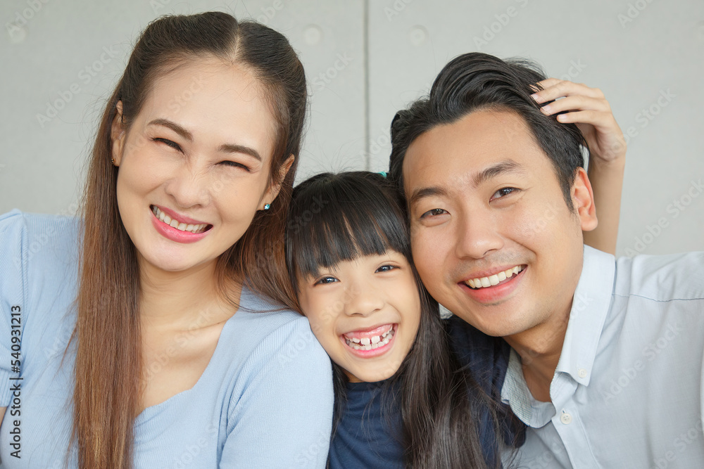 Portrait of a happy young family. Mom, dad and daughter look each other and smile. The faces of Asian parents and their child in living room. Portrait of a happy young family. Mom, dad and daughter look each other and smile. The faces of Asian parents and their child in living room.