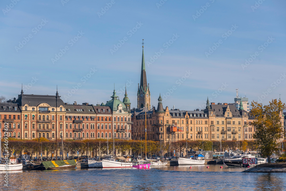 Fototapeta premium Panorama view, old fishing boats in the bay Ladugårdsviken with offices, apartment and hotel buildings a colorful autumn day in Stockholm