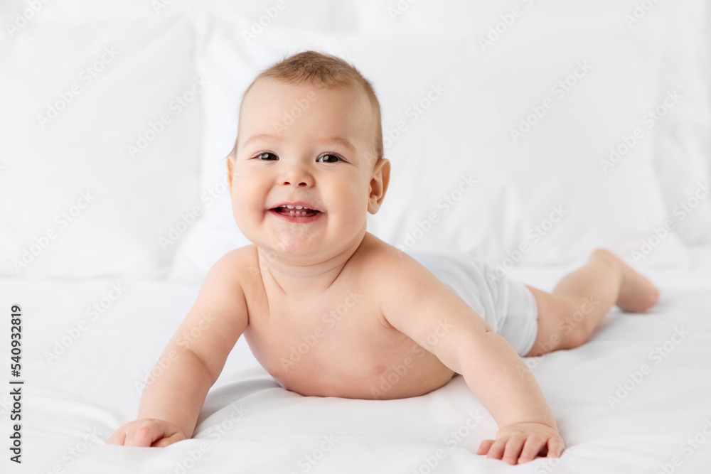 Smiling baby boy lying on stomach on white bed Smiling baby boy lying on stomach on white bed