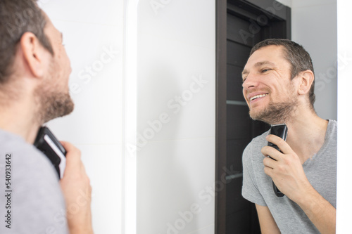 A happy man shaves and looks in the mirror