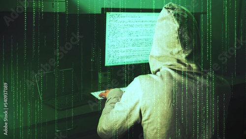 Teenage hacker in hoody works on desktop computer. Data code on display screen