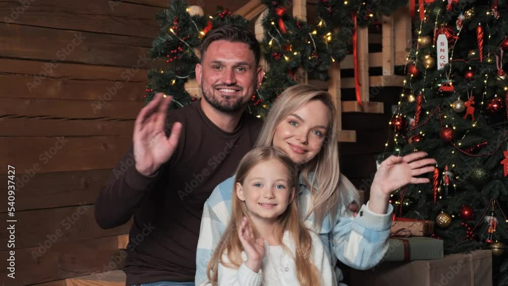Happy cheerful family posing for photo waving hands near christmas tree enjoying festive winter holiday at home. Mother, father, little girl pose say hello looking to the camera. New Year. Portrait. Happy cheerful family posing for photo waving hands near christmas tree enjoying festive winter holiday at home. Mother, father, little girl pose say hello looking to the camera. New Year. Portrait.