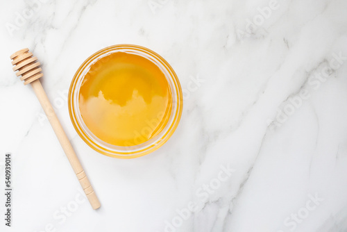 Honey in a bowl and a spoon for honey on a marble background. Copy space. Place for text. Top view. Flat lay.