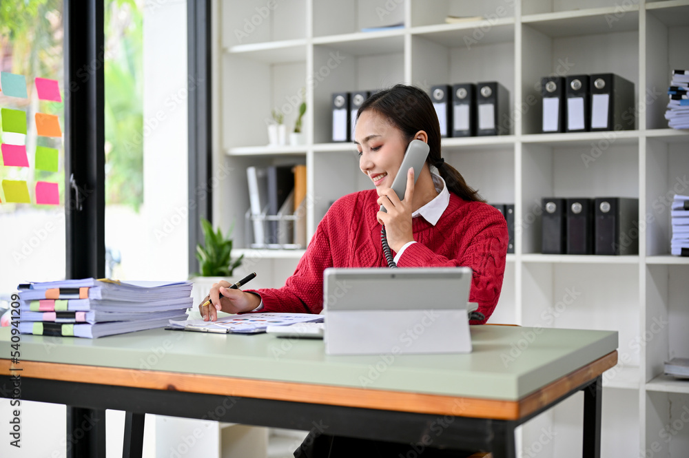 Beautiful Asian businesswoman or female secretary talking on the phone at her desk. Beautiful Asian businesswoman or female secretary talking on the phone at her desk.