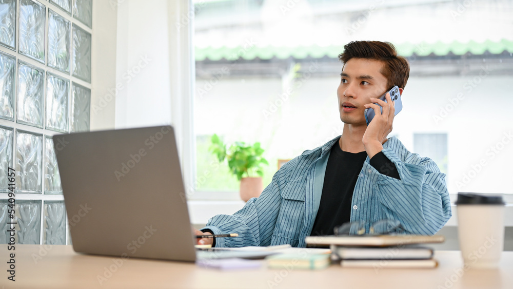 Professional Asian male office employee talking on the phone with his client while working Professional Asian male office employee talking on the phone with his client while working