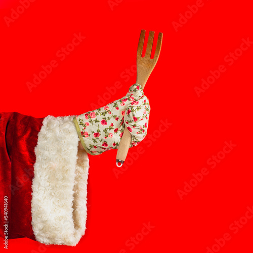 Christmas cooking and tasting. Festive meals concept. Santa Claus's hand in a kitchen glove holds a wooden fork.