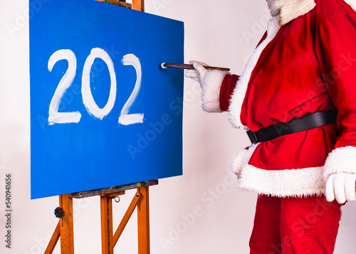 Happy New Year 2023- holiday greeting. Santa Claus in the image of an artist writes the numbers 202.