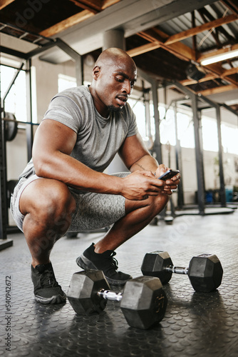 Fitness, phone and online personal trainer at the gym typing or searching on social media in Nigeria. Strong black man, bodybuilder and healthy sportsman networking or texting a digital message