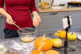 The girl shows the nakamra how to cook a cake for the holiday. Woman preparing dessert for thanksgiving and halloween. Blogger filming the process of making pumpkin pie on his phone