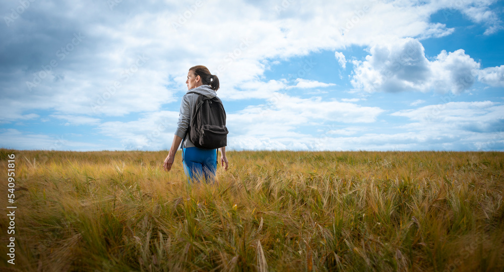 Woman with a backpack walking through a field, enjoying the countryside.