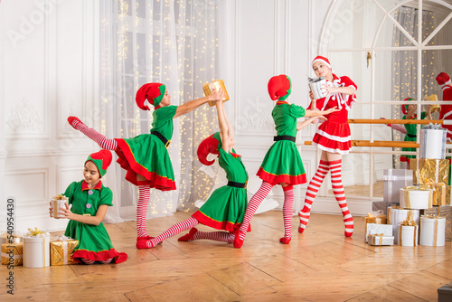 A group of cheerful happy children girls girlfriends students of a professional choreographic school in elf costumes dance with gifts against the background of a Christmas tree
