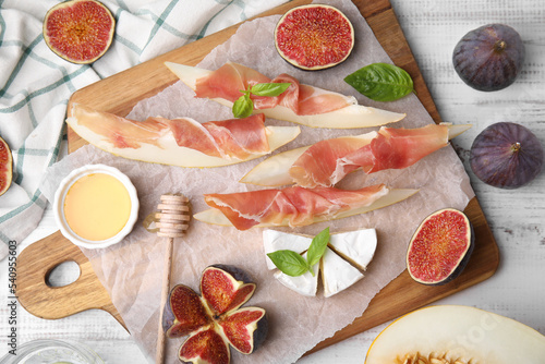 Tasty melon, jamon and figs served on white wooden table, flat lay