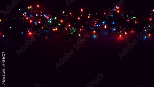 Flat lay glowing Christmas lights with copy space on dark plank background. Shot in 4k resolution. Multicolored Abstract Bokeh Background. Festive background with space for text. 