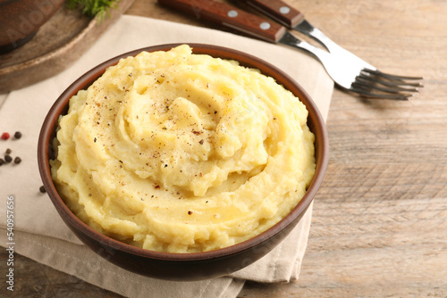 Bowl of tasty mashed potatoes with black pepper served on wooden table