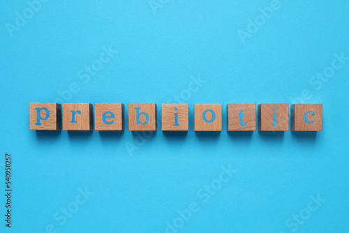 Wooden cubes with word Prebiotic on light blue background, flat lay