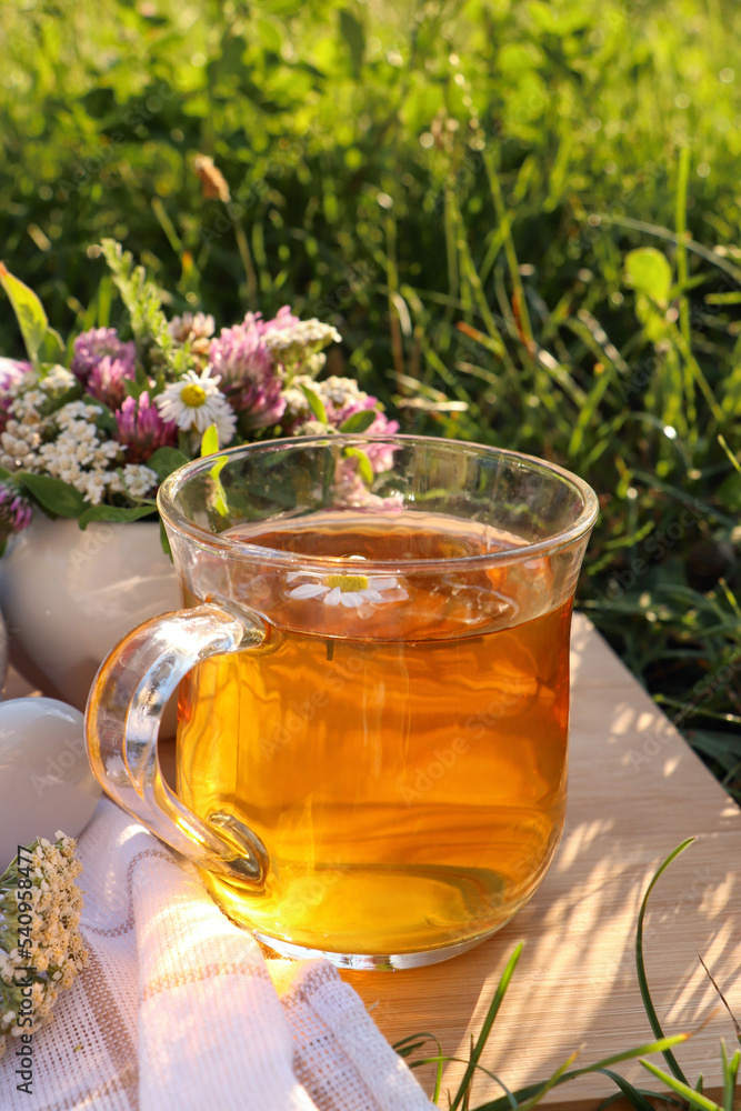 Cup of aromatic herbal tea and ceramic mortar with different wildflowers on wooden board in meadow Cup of aromatic herbal tea and ceramic mortar with different wildflowers on wooden board in meadow