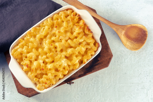 Macaroni and cheese pasta in a casserole dish, shot from the top with a wooden spoon and a place for text. Cheesy American gratin with noodles, baked in the oven