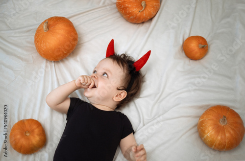 Cute year-old funny baby boy dressed as a devil horns with pumpkins