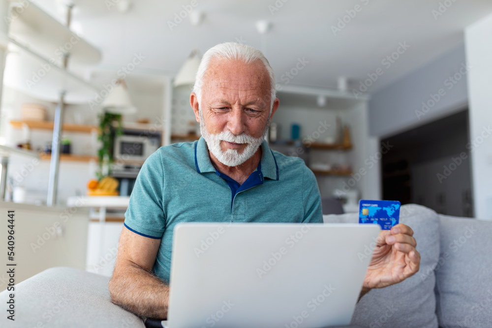 Mature man using laptop, holding plastic credit or debit card, senior grey haired customer making secure internet payment, shopping or browsing online banking service, entering information Mature man using laptop, holding plastic credit or debit card, senior grey haired customer making secure internet payment, shopping or browsing online banking service, entering information