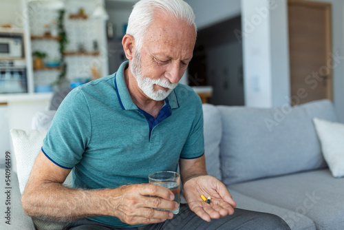 Fotografie Senior man takes pill with glass of water in hand