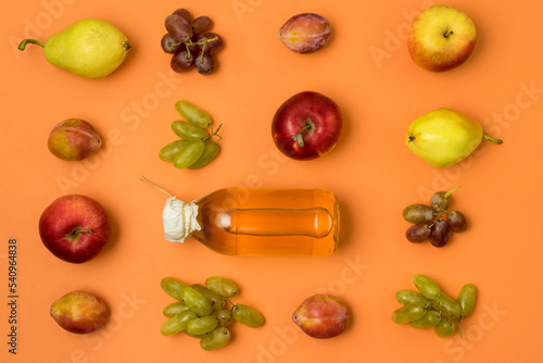 Bottle With Apple Cider or Vinegar with Raw Autumn Fruits Grape Apples Pears Plums on Orange Background Top View Horizontal
