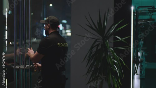 Guard or security worker walking , closing door and turning  plate with open closed sign at night . Guard dressed security uniform working inside storage or shop . Concept of night shift work